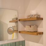 Badezimmer mit Holzregalen, Spiegel und grünen Fliesen.
