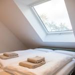Schlafzimmer mit Dachfenster und Blick auf Bäume. Bett mit weißen Laken und gefalteten Handtüchern.