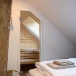 Schlafzimmer mit Blick in eine Holzsauna mit Sitzbänken.