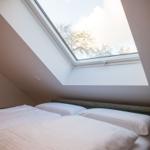 Schlafzimmer mit Dachschrägen und Dachfenster, Blick auf Bäume.