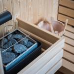 Sauna mit Steinmulde, Holzbank und Eimer mit Löffel.