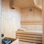 Sauna mit Holzbank, Wanduhr und Steinkasten.
