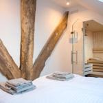 Schlafzimmer mit Bett, Holzpfosten und Sauna im Hintergrund.