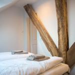 Zimmer mit zwei Betten und rustikalen Holzbalken an der Wand.