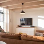 Wohnzimmer mit braunem Sofa, Fernseher und Holzbalkendecke.