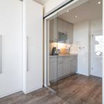 Küche mit Glaswand und weißen Schränken. Holzfußboden und moderne Einbauküche.