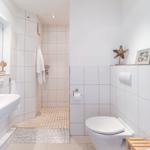 Badezimmer mit Dusche, Waschbecken und Toilette. Weiße Fliesen und dekorative Elemente.