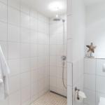 Dusche mit Duschbrause, Toilette und Handtuch an der Wand.