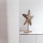 Holzstern auf Standfuß neben Bild mit Muscheln und Steinen.