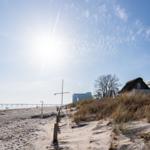 Strand mit Dünen, Hütte und Pier unter blauem Himmel.