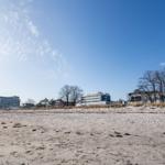 Strand mit Sand und Gebäuden im Hintergrund unter blauem Himmel.