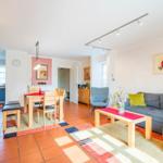 Wohn- und Essbereich mit Sofa, Tisch und Stühlen. Terrakottaboden und Holzmöbel.