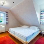 Schlafzimmer mit Dachschrägen, Bett, zwei Fenstern und Teppichen.