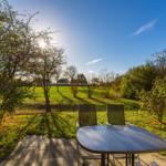 Terrasse mit Tisch und Stühlen im Garten unter blauem Himmel.