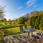 Terrasse mit Tisch und Stühlen, Blick auf grünen Garten und Hecken.