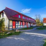 Ferienhaus mit Fachwerk, rotem Dach und orangefarbenen Türen. Grünflächen und Steine im Vorgarten.
