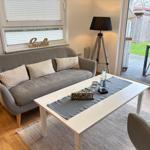 Ein Wohnzimmer mit grauem Sofa, weißem Tisch und Blick auf die Terrasse.
