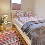 Schlafzimmer mit Bett, Nachttisch und buntem Teppich.