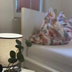 Schlafzimmer mit Bett, Nachttisch und Lampe. Fenster mit Jalousie im Hintergrund.