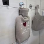 Wärmflasche mit Aufschrift hängt an Wandhalterung im Badezimmer.