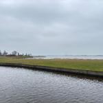 Wasserkanal mit Grasfläche und Blick auf See und rote Häuser.