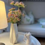 Auf dem Nachttisch steht eine weiße Vase mit Blumen und eine Katzenfigur.