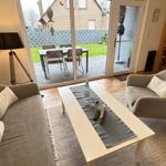 Wohnzimmer mit Sofa, Sessel und Tisch. Durchgang zur Terrasse mit Tisch und Stühlen.