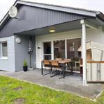 Haus mit Terrasse, Tisch, Stühlen und Strandkorb. Außenbereich mit Pflanze und Satellitenschüssel.