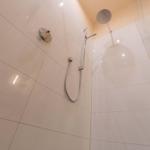 Dusche mit Duschbrause und Handbrause an glatten Fliesenwänden.