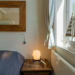 Bett mit Nachttisch, Spiegel und Segelschiffmodell am Fenster