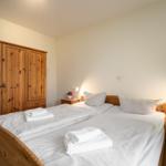 Zimmer mit Doppelbett, Holzkommode und Nachttischen mit Lampen.