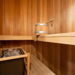 Sauna mit Holzbank, Steinofen und Holzeimer.