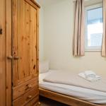 Schlafzimmer mit Holzschrank, Bett und Fenster mit Vorhängen.