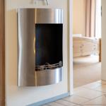 Wandmontierte Feuerstelle mit Holz im Flur. Im Hintergrund ist ein Schlafzimmer mit Bett sichtbar.