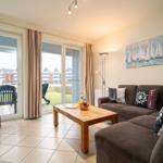 Wohnzimmer mit Sofa, Couchtisch und TV. Durchgang zum Balkon mit Sicht auf Wohnhäuser.