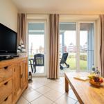 Wohnzimmer mit Fernseher, Holztisch und Blick auf die Terrasse.