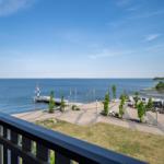 Blick vom Balkon auf See, Pier und Strandbereich mit Sitzgelegenheiten.