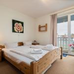 Schlafzimmer mit Holzbett, Nachttisch und Balkonansicht.