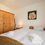 Schlafzimmer mit Holzbett, Kleiderschrank und Nachttisch. Auf dem Bett liegen gefaltete Handtücher.
