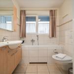 Bad mit Badewanne, Waschbecken und Toilette. Fenster mit Vorhängen.
