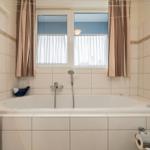 Bad mit Badewanne, Fenster und Holzschränken.