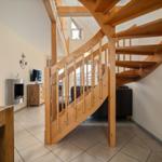 Holzspindeltreppe führt zur oberen Etage. Im Hintergrund Wohnzimmer mit Sofa und Fernseher.