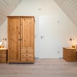 Zimmer mit zwei Betten, Holzschrank und Schreibtisch unter schrägen Dachschrägen.