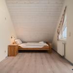 Schlafzimmer mit Holzbett, Schrank und Fenster. Dachschräge und Holzfußboden.