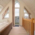 Dachgeschosszimmer mit Bett, Fenstern und Balkonzugang.