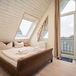 Schlafzimmer mit Dachschrägen, Bett, Fenster und Balkonzugang.