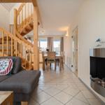 Wohnzimmer mit Sofa, Kamin und Holztreppe zur oberen Etage.