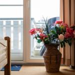 Ein Bett neben einem Fenster mit Blumen in einem Korb. Draußen ist eine Terrasse.