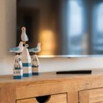 Holzkommode mit Vogeldekoration und Fernseher im Hintergrund.
