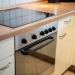 Küche mit Induktionskochfeld und Backofen. Holzoberfläche und weiße Schränke.